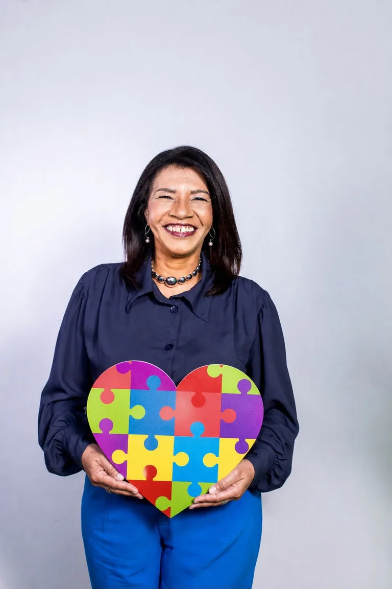 Cris Almeida, a Tia Cris, segurando um coração de quebra-cabeça, símbolo do autismo